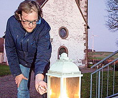 Zündet für die Aktion „Licht der Hoffnung“ ein Licht auf der Treppe des Pfarrheims an: Pfarrer Mathias Müller aus Rothselberg. Foto: Sayer