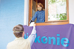 Das Fenster als coronakonforme Bargeldschleuse: Heidi Berlitz demonstriert in Otterbach in einer gestellten Szene wie die Bargeldübergabe abläuft. Foto: view